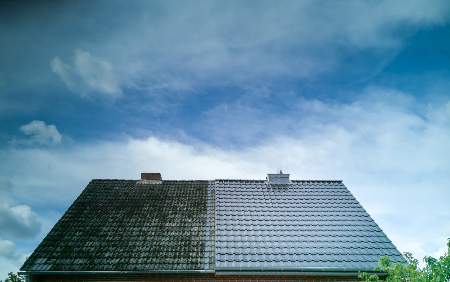 A half cleaned house roof shows the before and after effect of a roof cleaning.